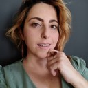 Camila Castro Camila possui pele branca, cabelos loiros e veste uma blusa verde.