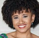 Gina Albuquerque Gina é negra, tem cabelos crespos e está sorrindo.